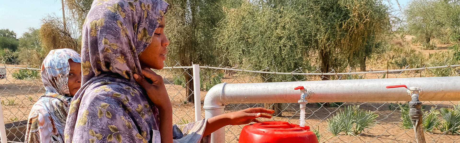 Zwei Frauen im sudanesischen Abu Hashim füllen Wasser in einen roten Kanister ab