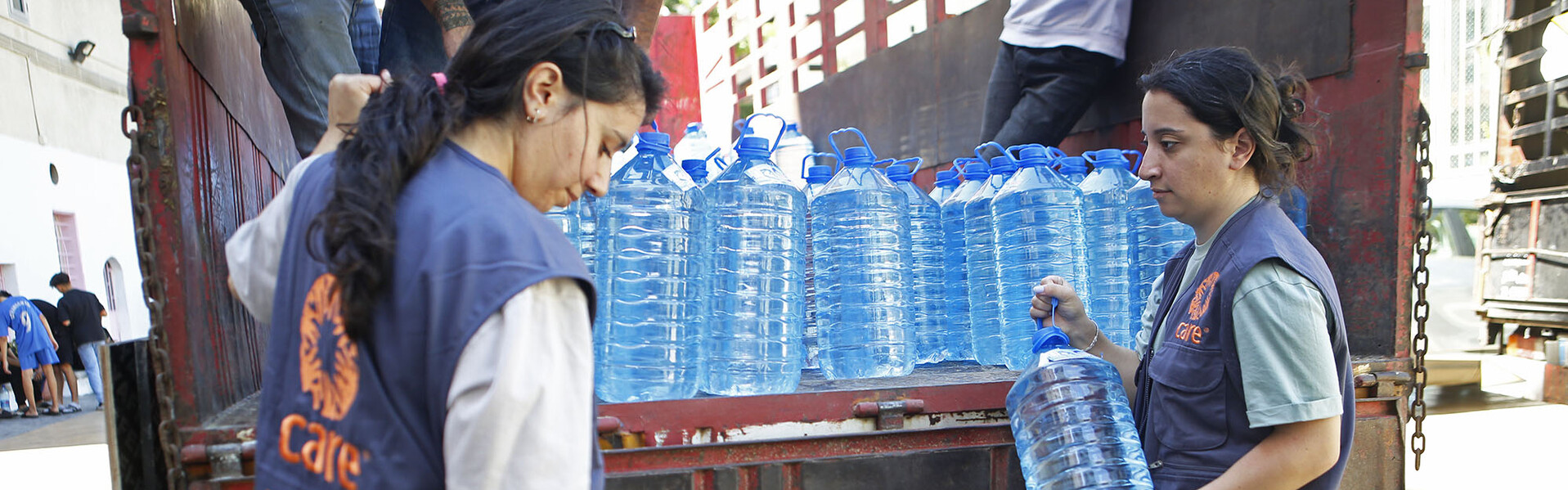 Helferinnen der Organisation CARE entladen einen LKW mit Trinkwasserflaschen