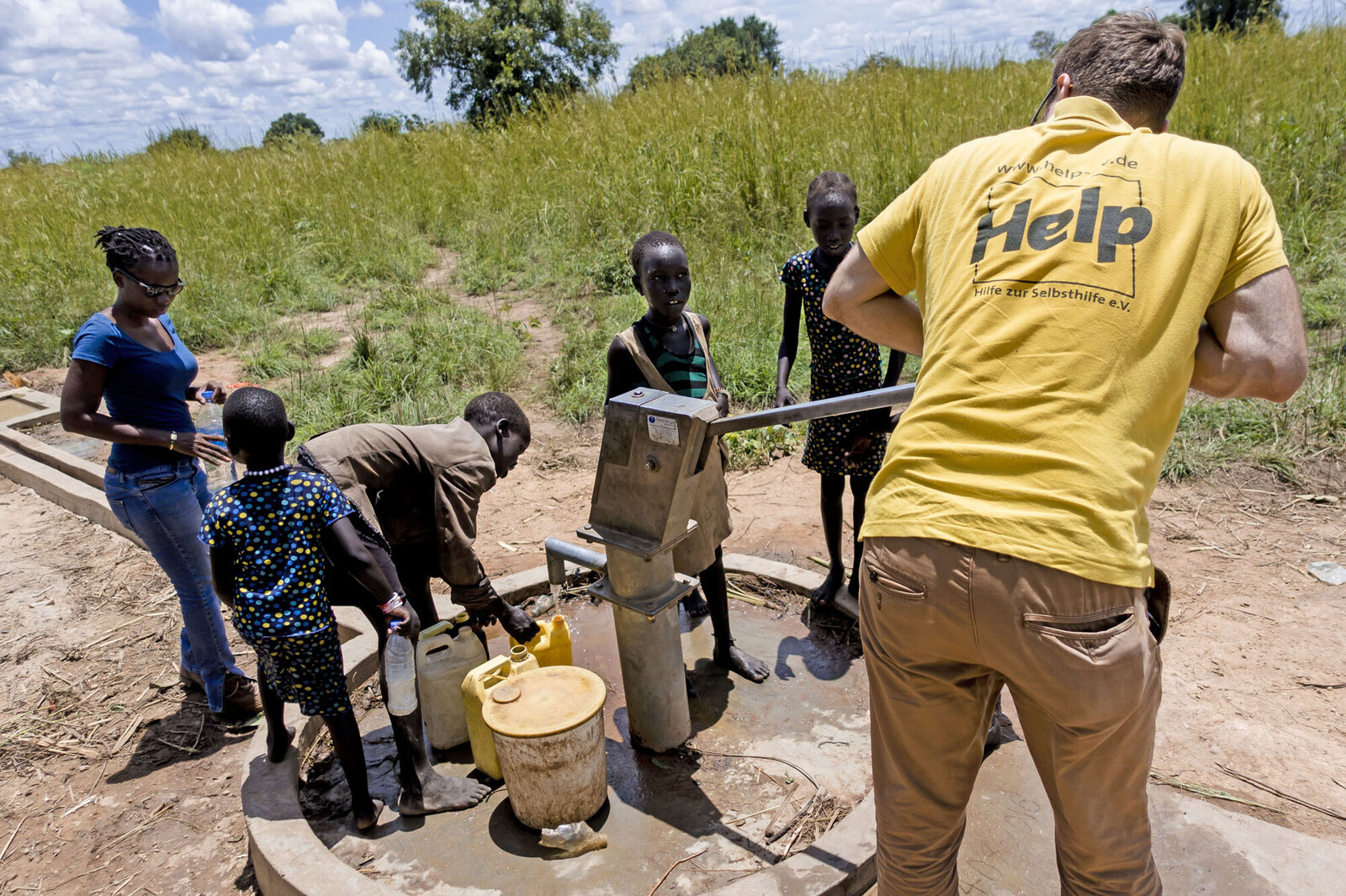 Ein Helfer unserer Bündnisorganisation Help mit Kindern an einem Brunnen in Afrika