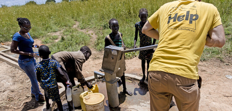 Ein Helfer unserer Bündnisorganisation Help mit Kindern an einem Brunnen in Afrika Ein Helfer unserer Bündnisorganisation Help mit Kindern an einem Brunnen in Afrika