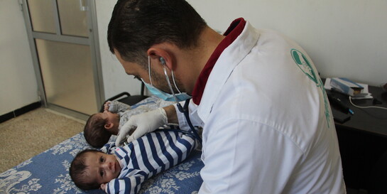 Ein Arzt mit Mundschutz und Stethoskop untersucht die im syrischen Bürgerkrieg geborenen Zwillinge Ahmed und Areej