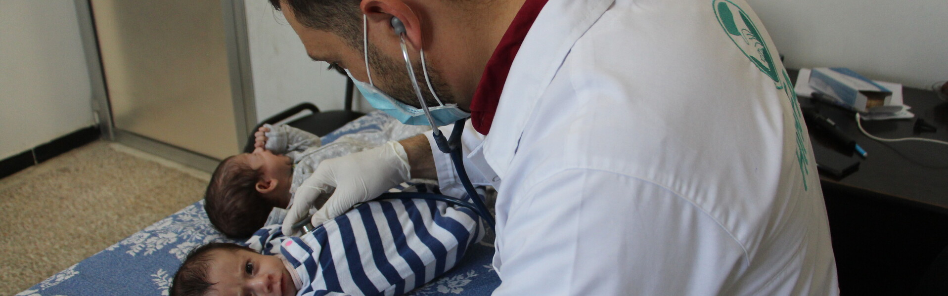 Ein Arzt mit Mundschutz und Stethoskop untersucht die im syrischen Bürgerkrieg geborenen Zwillinge Ahmed und Areej