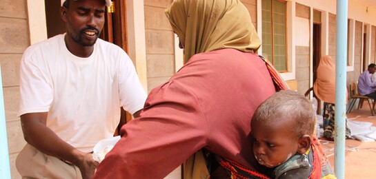 Helfer gibt Frau und Kind eine Tüte im FLüchtlingslager in Dadaab