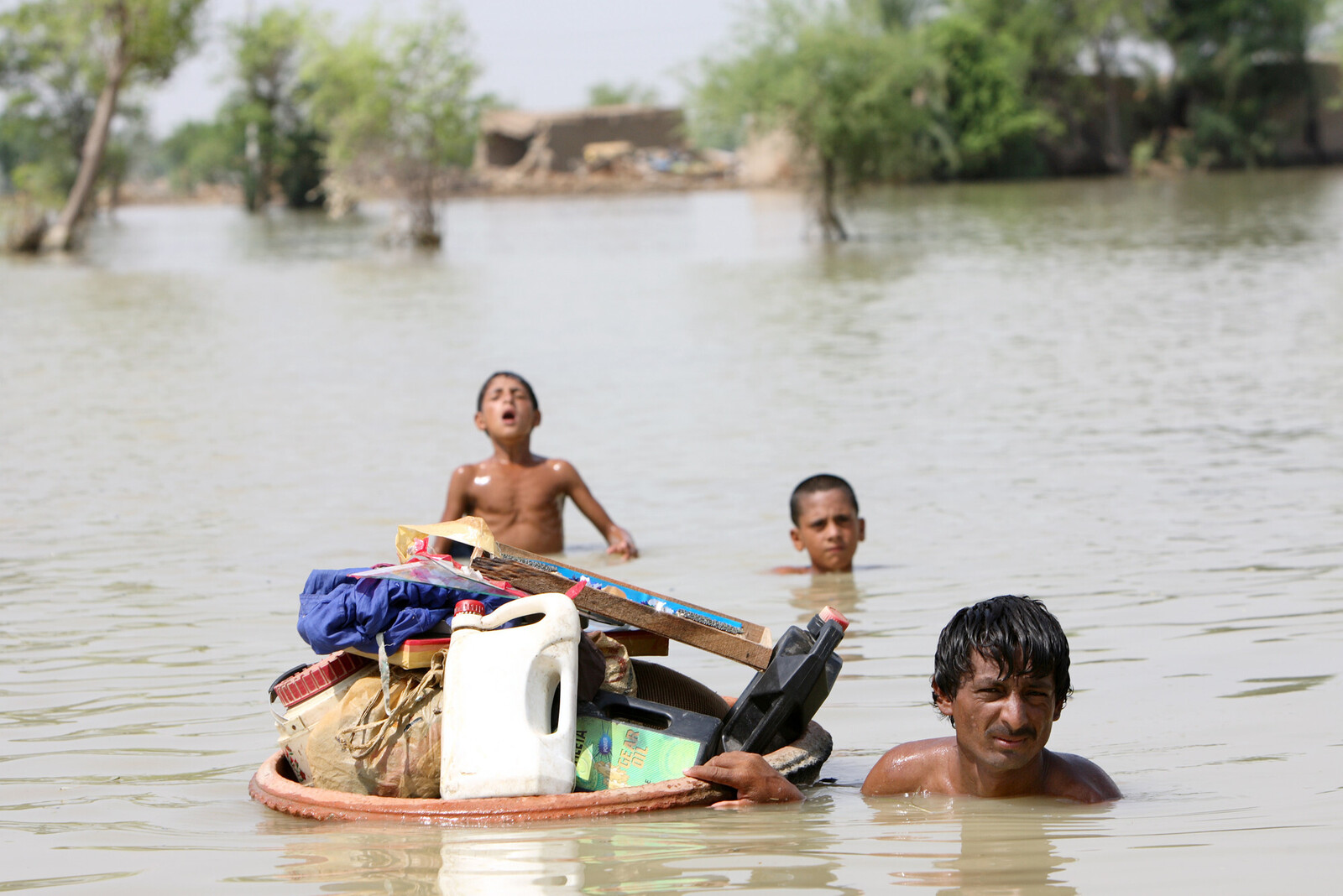 Ein Vater mit seinen zwei Söhnen retten ihre Habseligkeiten vor den Fluten in Pakistan