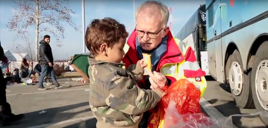 Ein Helfer vom ASB gibt einem Flüchtlingskind ein Schokoriegel in Serbien.
