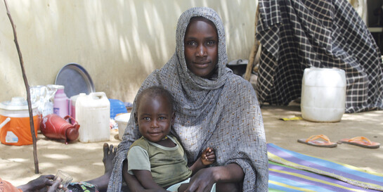 Eine Mutter aus dem Sudan sitzt mit ihrem Kind im Arm auf einem Teppich