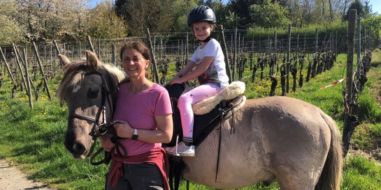 Ein Mädchen sitzt auf einem Pferd, begleitet von einer Reitlehrerin
