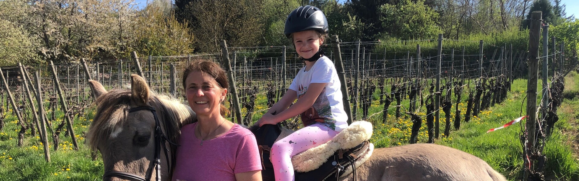 Ein Mädchen sitzt auf einem Pferd, begleitet von einer Reitlehrerin