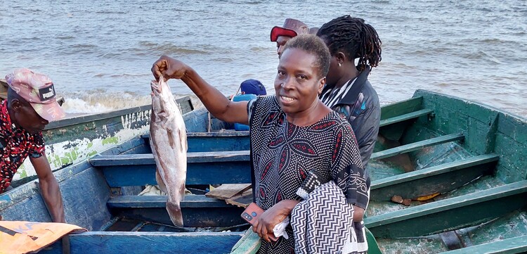 Eine Frau steht in einem Boot und hält einen Fisch Eine Frau steht in einem Boot und hält einen Fisch