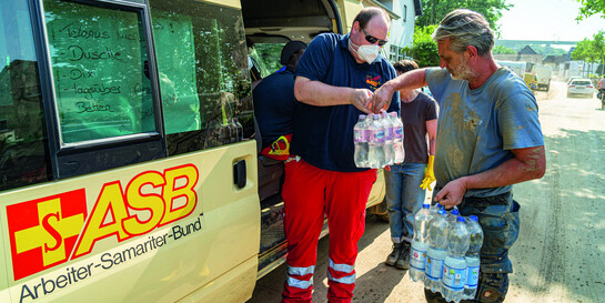 Ein Helfer vom ASB überreicht einem Mann Wasserflaschen