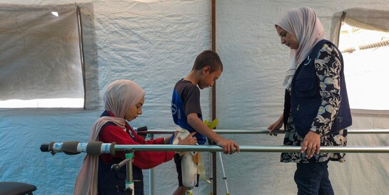 Zwei Helferinnen von Handicap International unterstützen einen Jungen bei der Reha