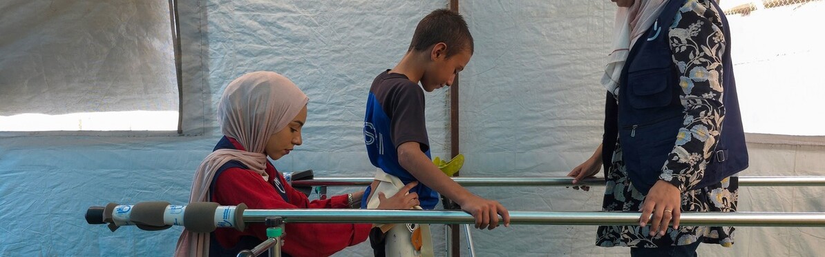 Zwei Helferinnen von Handicap International unterstützen einen Jungen bei der Reha