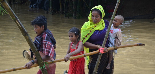 Eine Familie überquert einen überfluteten Weg im Flüchtlingsamp in Bangladesh.