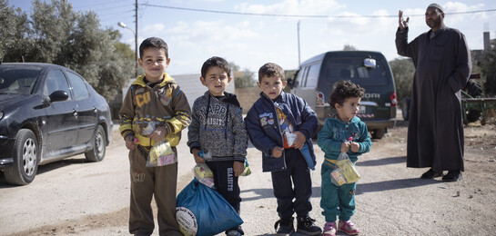 Kinder stehen auf der Straße. Ein Mann erzählt eine Geschichte. Die Kinder sind Flüchtlinge in Jordanien