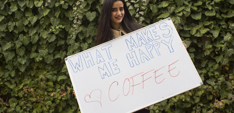 Frau hält ein Schild hoch mit der Aufschrift "#whatmakesmehappy". Kaffee macht sie glücklich