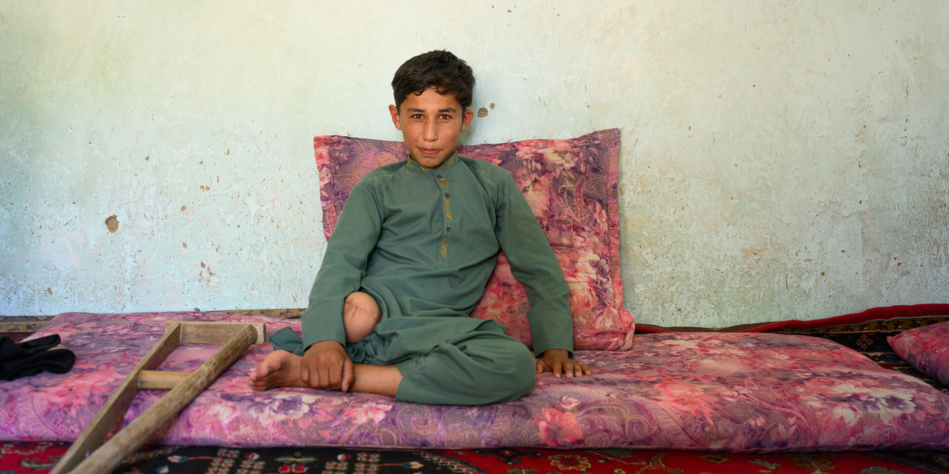 Omaid aus Afghanistan sitzt auf einer Matte, neben ihm liegt seine Gehhilfe Omaid aus Afghanistan sitzt auf einer Matte, neben ihm liegt seine Gehhilfe