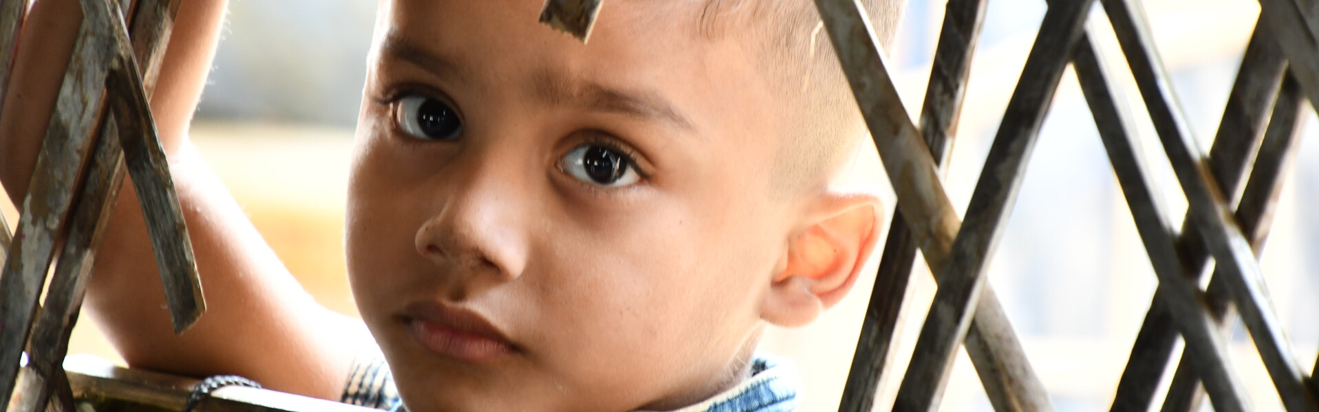 Ein Junge in Bangladesch, hinter einem Zaun