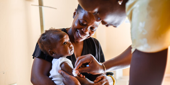 Eine Krankenschwester in Haiti impft ein Kleinkind, das in dem Armen seiner Mutter sitzt