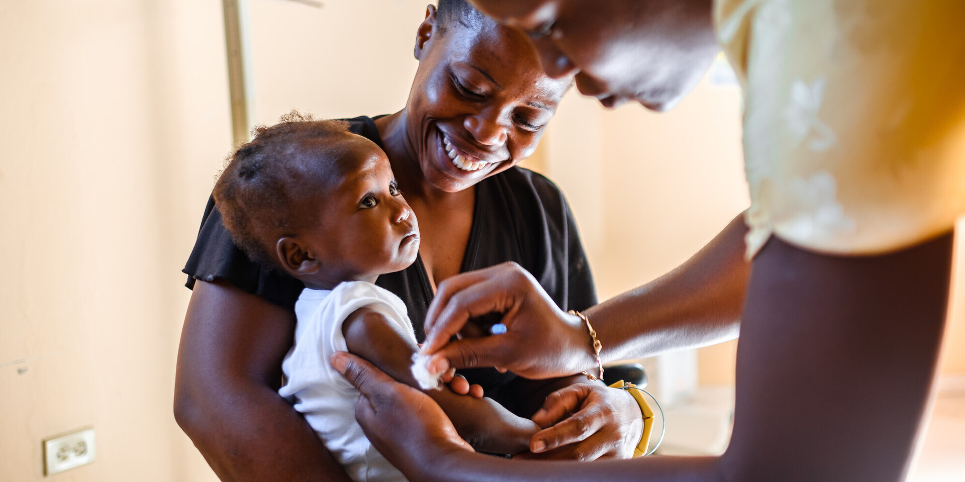 Eine Krankenschwester in Haiti impft ein Kleinkind, das in dem Armen seiner Mutter sitzt