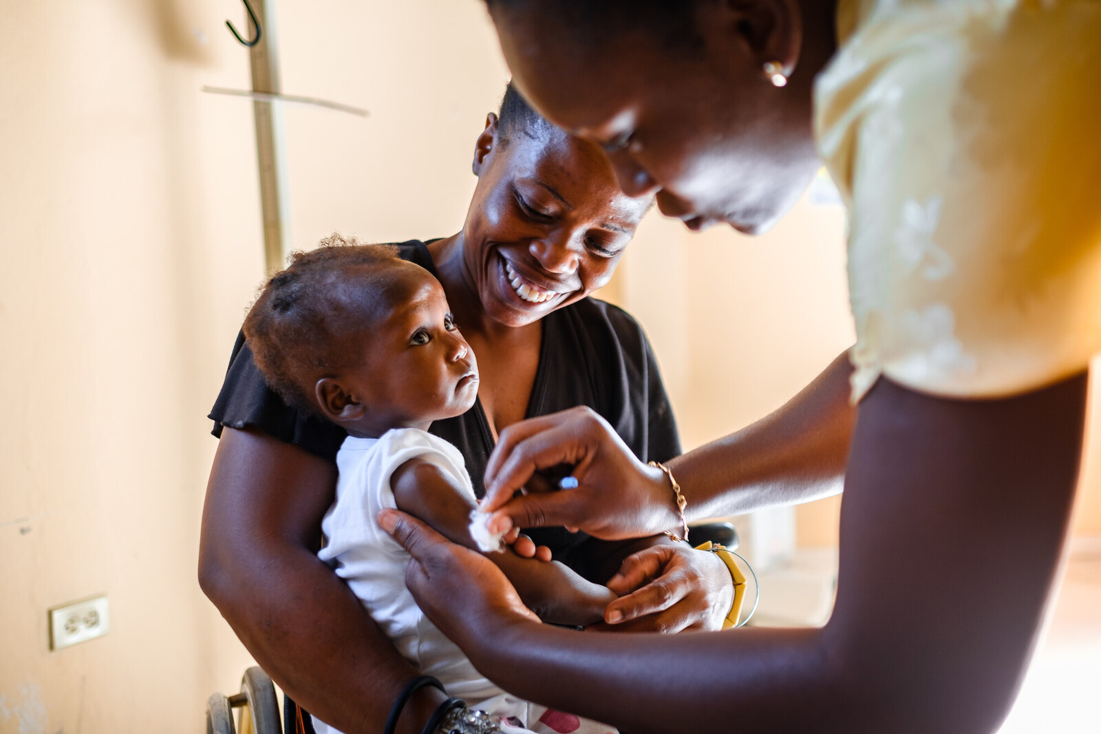Eine Krankenschwester in Haiti impft ein Kleinkind, das in dem Armen seiner Mutter sitzt