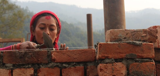 Die Maurerin Kopila baut die Mauer eines Hauses in Nepal wieder auf. 