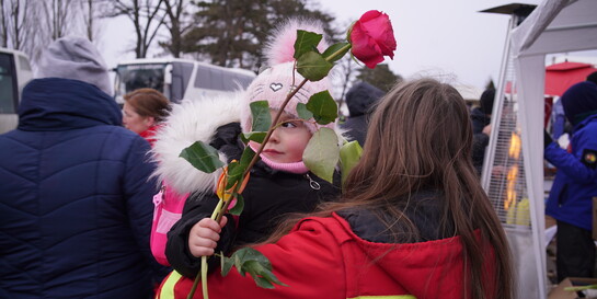 Eine Helferin trägt ein Mädchen, das eine Rose in der Hand hält