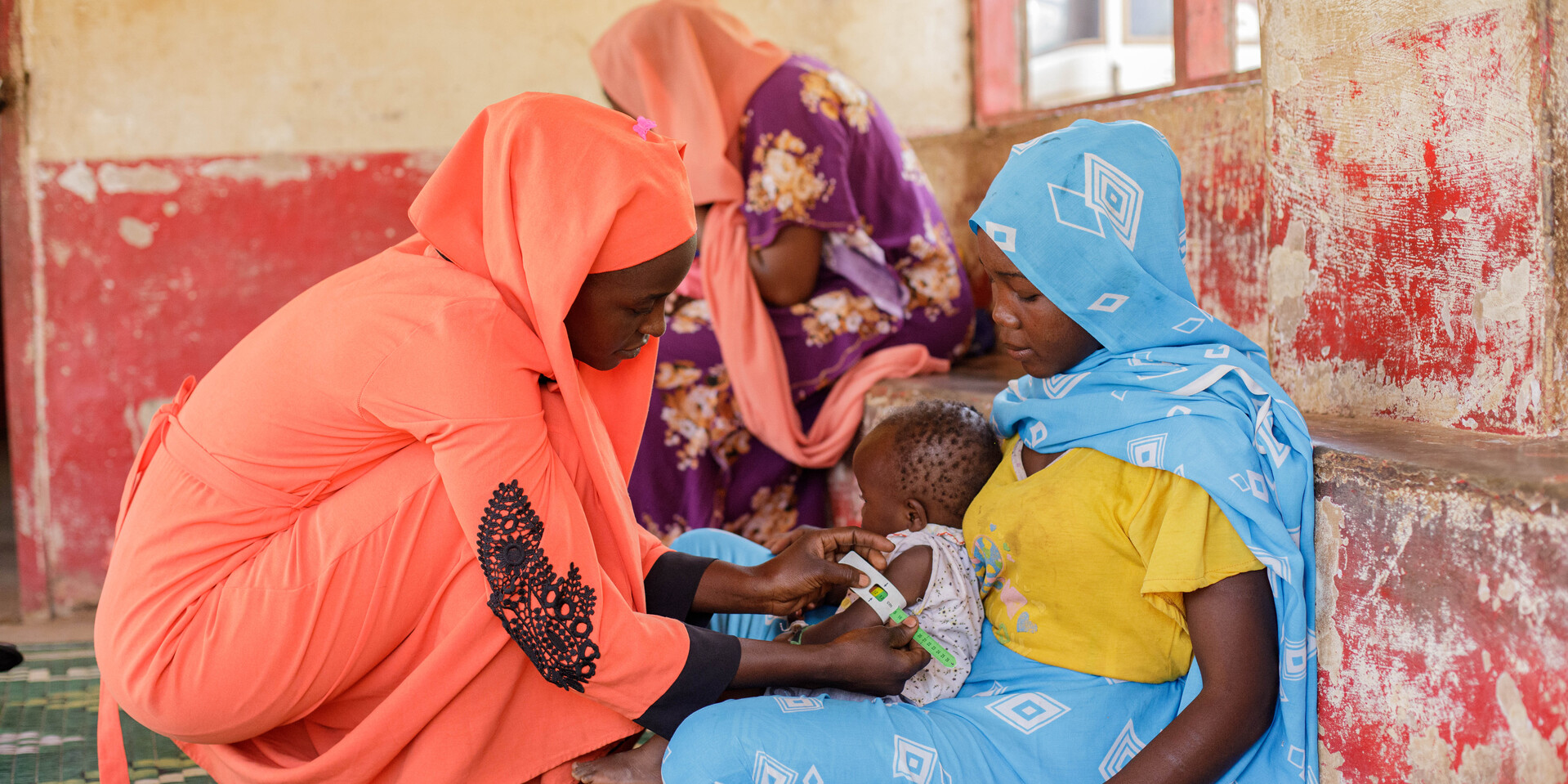 Eine Frau in einem Geflüchtetencamp im Südsudan untersucht ein Kind auf dem Schoß seiner Mutter auf Unterernährung