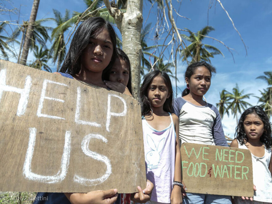 An den Straßenrändern stehen Kinder und halten selbst bemalte Schilder hoch