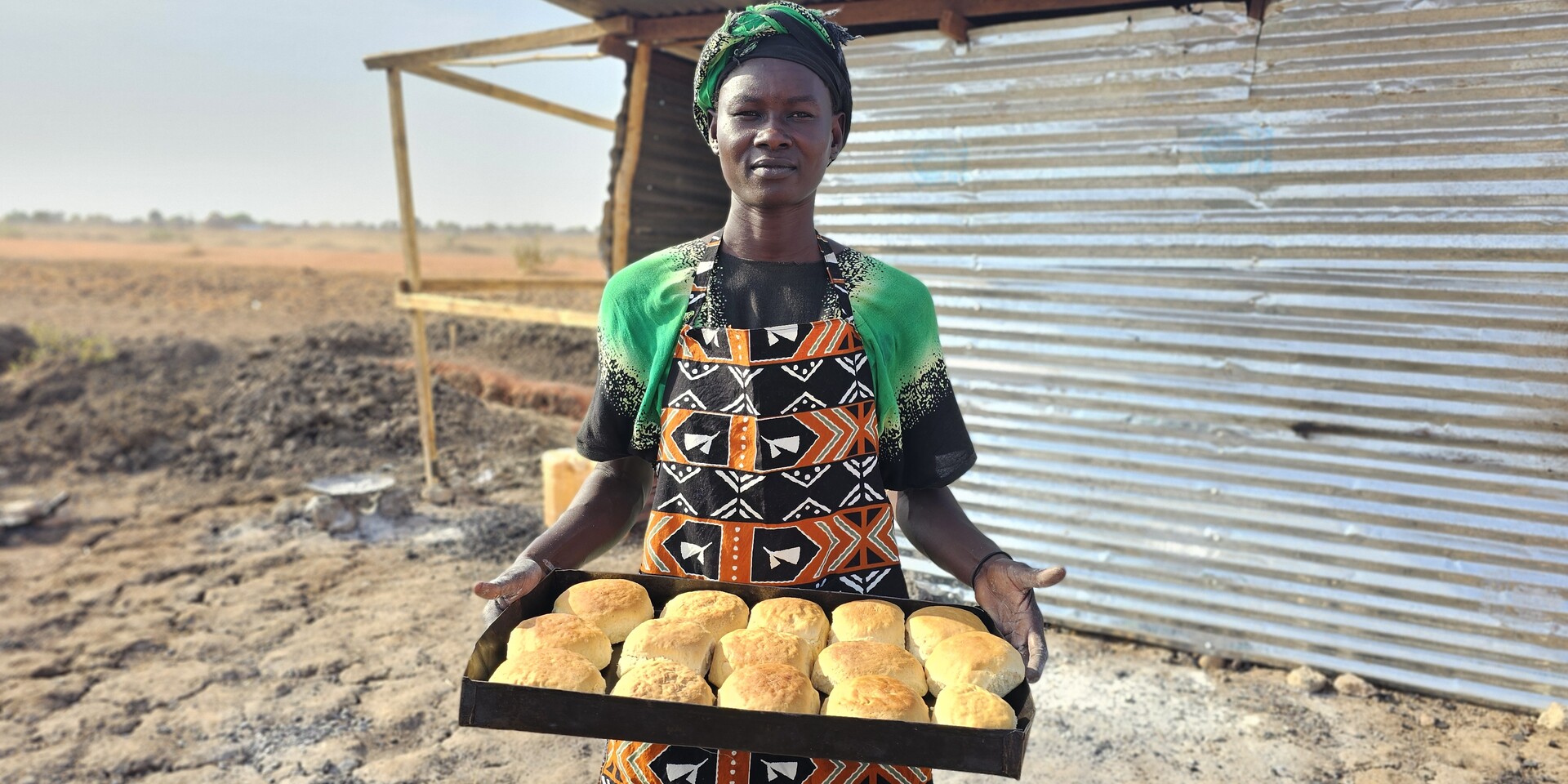 Nyabol hält ein Blech mit frischen Broten in den Händen