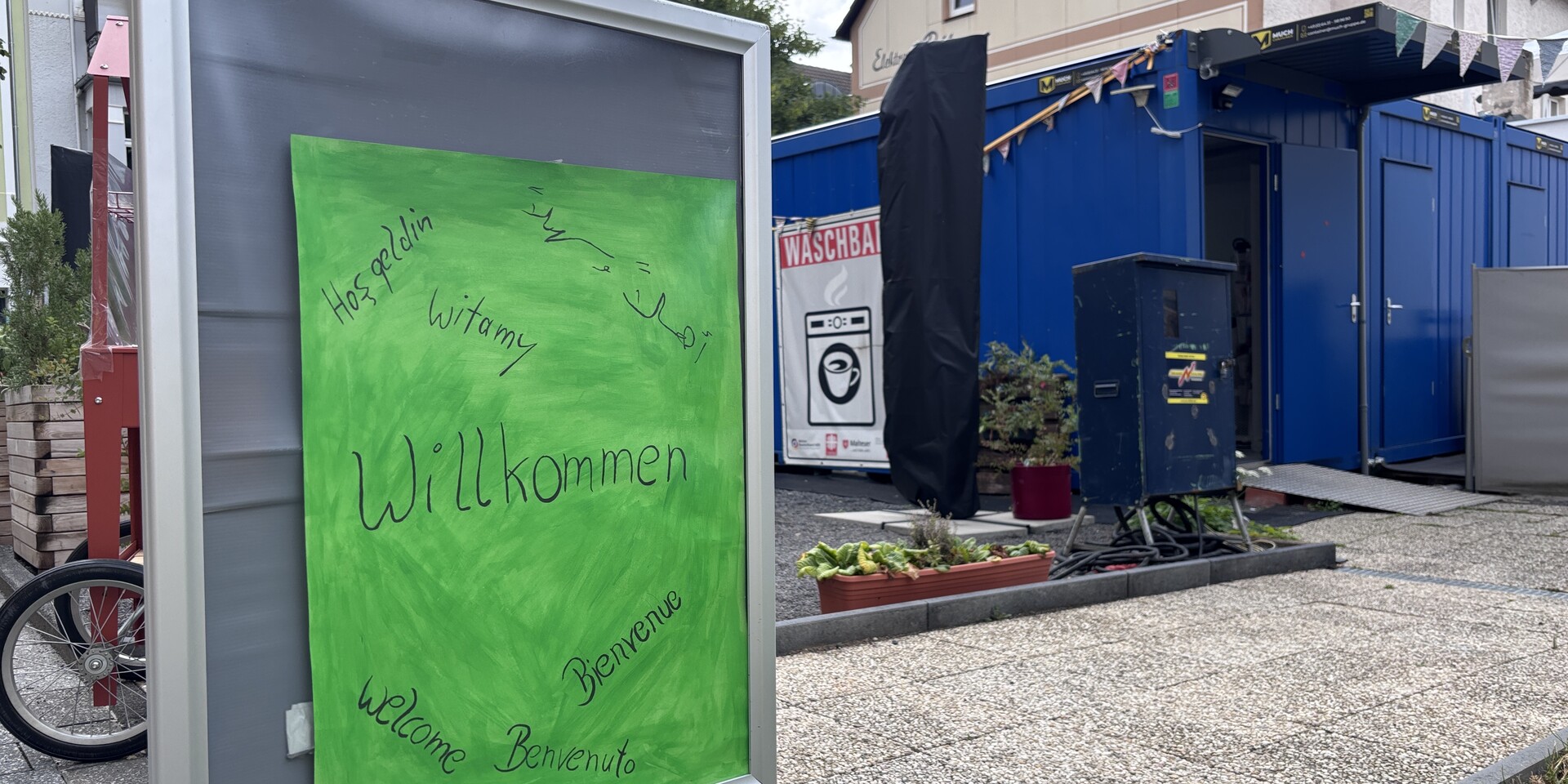 Ein Willkommen-Schild steht vor einem der Container der Waschbar