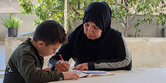 Eine Frau macht mit einem Jungen in Syrien zusammen seine Hausaufgaben