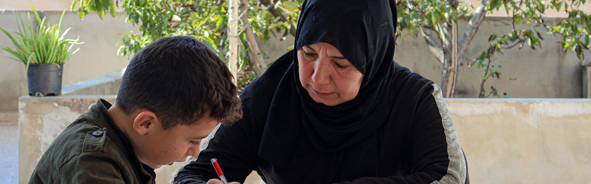 Eine Frau macht mit einem Jungen in Syrien zusammen seine Hausaufgaben