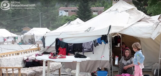 Flüchtlinge sitzen vor einem Zelt.