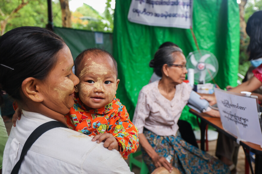 Eine Frau steht mit einem Baby im Arm vor einer Gesundheitsstation in Myanmar