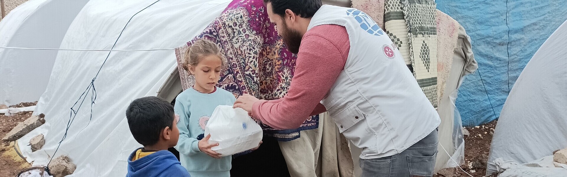 Ein Helfer von einer Partnerorganisation der Johanniter verteilt Lebensmittel an obdachlose Kinder im Erdbebengebiet Türkei-Syrien