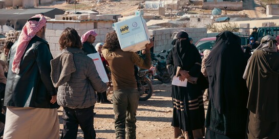 Ein Helfer von Help in einer Gruppe von Menschen verteilt Hilfspakete in Syrien