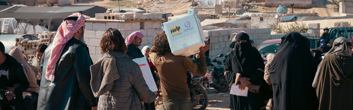 Ein Helfer von Help in einer Gruppe von Menschen verteilt Hilfspakete in Syrien