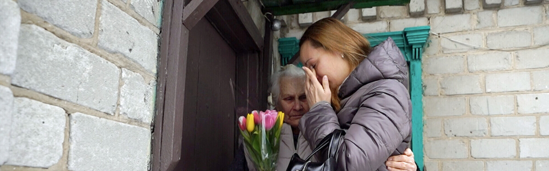 Eine ältere Frau mit einem Strauß Tulpen umarmt eine jüngere Frau, die weint