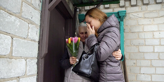 Eine ältere Frau mit einem Strauß Tulpen umarmt eine jüngere Frau, die weint