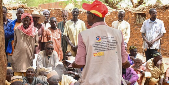 Ein Helfer von ASB steht im Niger vor einer Menschengruppe
