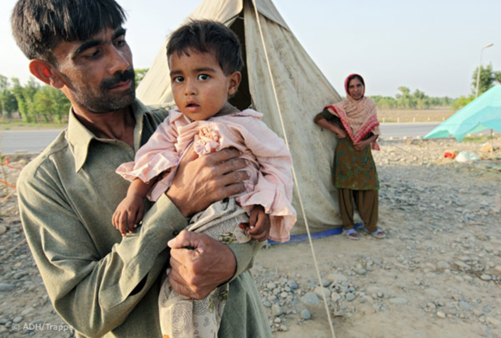 2010.08.27-vater-kind-an-autobahn Flut Pakistan:27.08.2010, Pakistan, Nowshera - Hochwasser Pakistan. Auf der Autobahnstrecke Richtung Peshawar campieren Flüchtlinge des Hochwassers in Zelten.