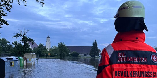Ein Helfer der Johanniter blickt auf das Hochwasser in einer Stadt in Bayern