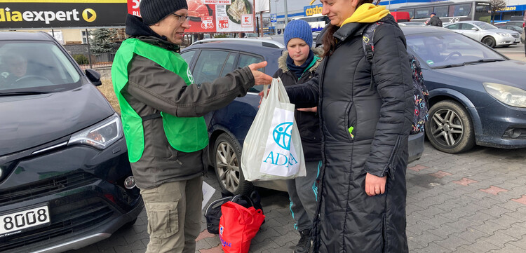 Ein Helfer von ADRA überreicht einer Frau eine Tüte mit Hilfsgütern