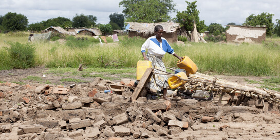 Eine Frau in Malawi mit Wasserkanistern auf ihrem zerstörten Acker