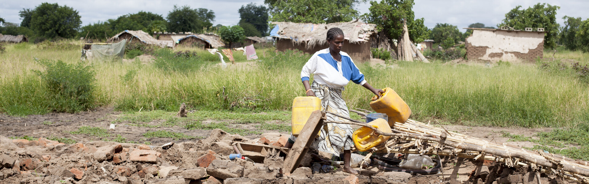 Eine Frau in Malawi mit Wasserkanistern auf ihrem zerstörten Acker