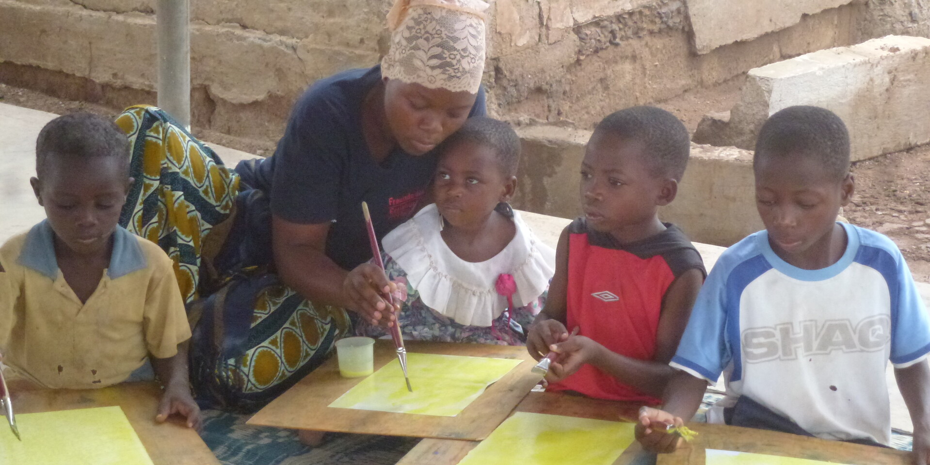 Eine Lehrerin im Kinderschutzzentrum des kenianischen Flüchtlingscamps Kakuma malt mit vier Kindern Aquarell-Bilder 