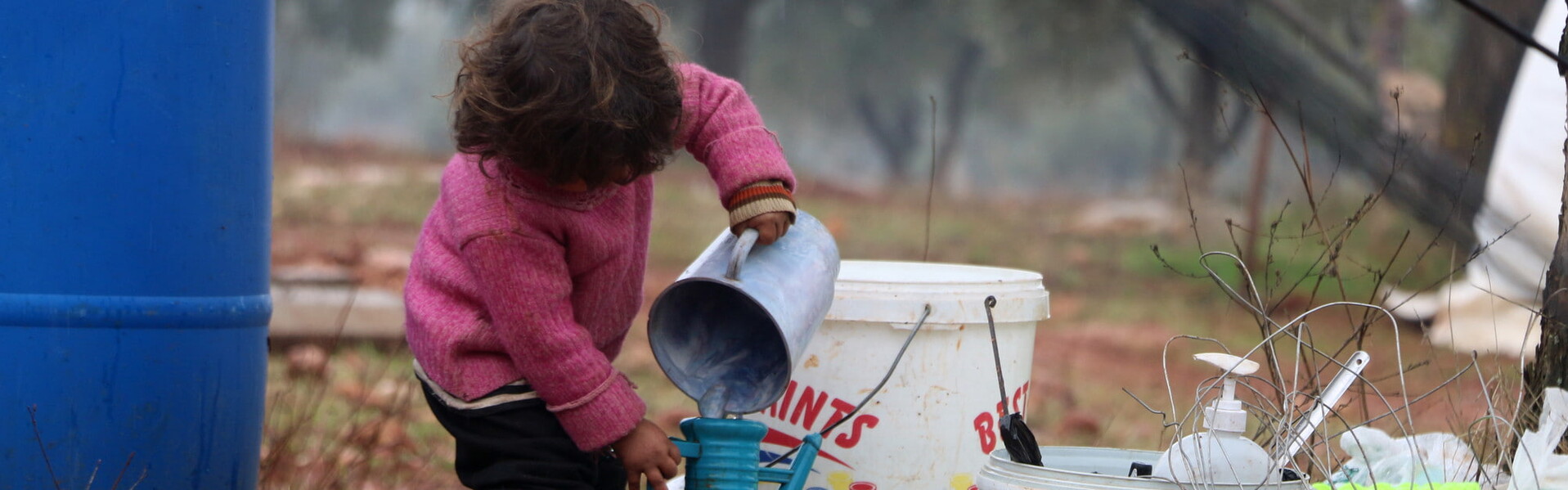 Ein Kind in einem Geflüchtetencamp in Syrien Ein Kind in einem Geflüchtetencamp in Syrien, das Wasser von einem Gefäß in ein anderes schüttet