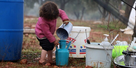 Ein Kind in einem Geflüchtetencamp in Syrien, das Wasser von einem Gefäß in ein anderes schüttet