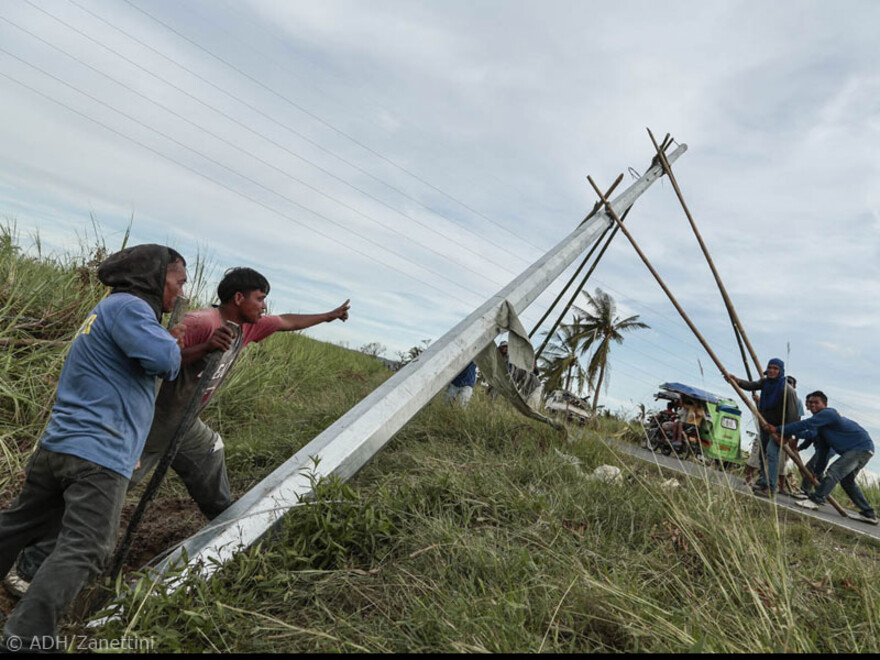 Hier stellen ein paar Männer mit vereinten Kräften einen Strommast auf
