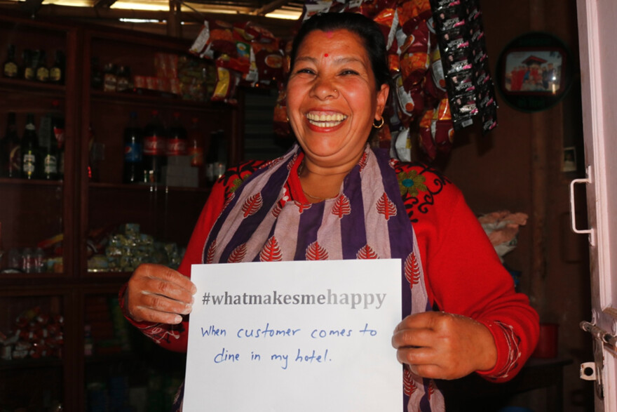 Frau hält in Nepal einen Zettel in einem Laden. Auf dem Zettel steht "whatmakesmehappy" und sie macht es glücklich, wenn Sie kunden im Geschäft hat.